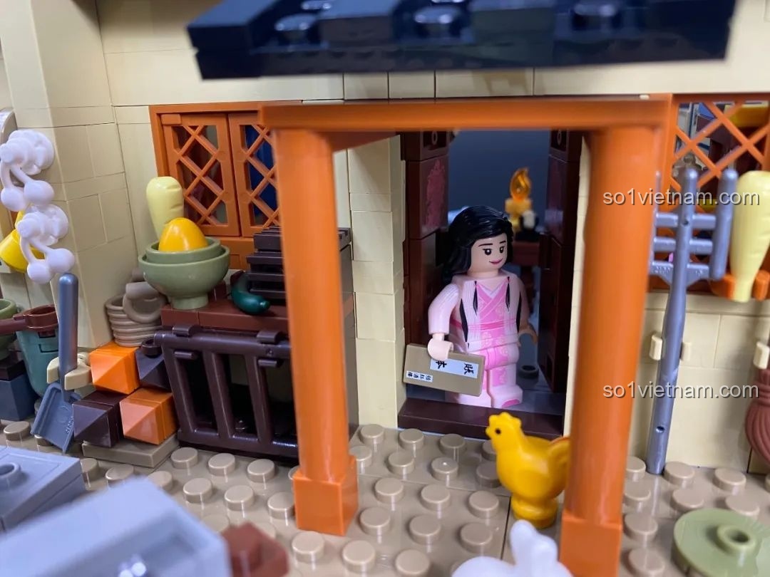 Cận cảnh một minifigure nữ đang bước ra từ cổng, bên cạnh là một chú gà.