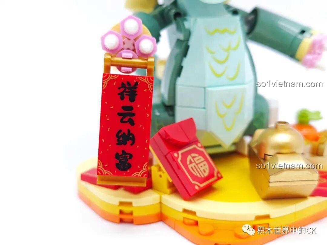 Cận cảnh câu đối và bao lì xì trên tay chú rồng xanh, mang ý nghĩa tài lộc.