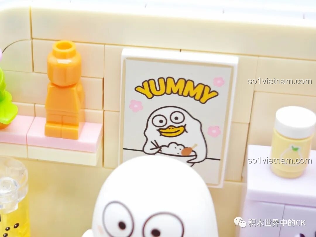 Chi tiết bông hoa trang trí màu tím và chai lọ màu cam trên kệ của mô hình Vịt Liu ăn uống.