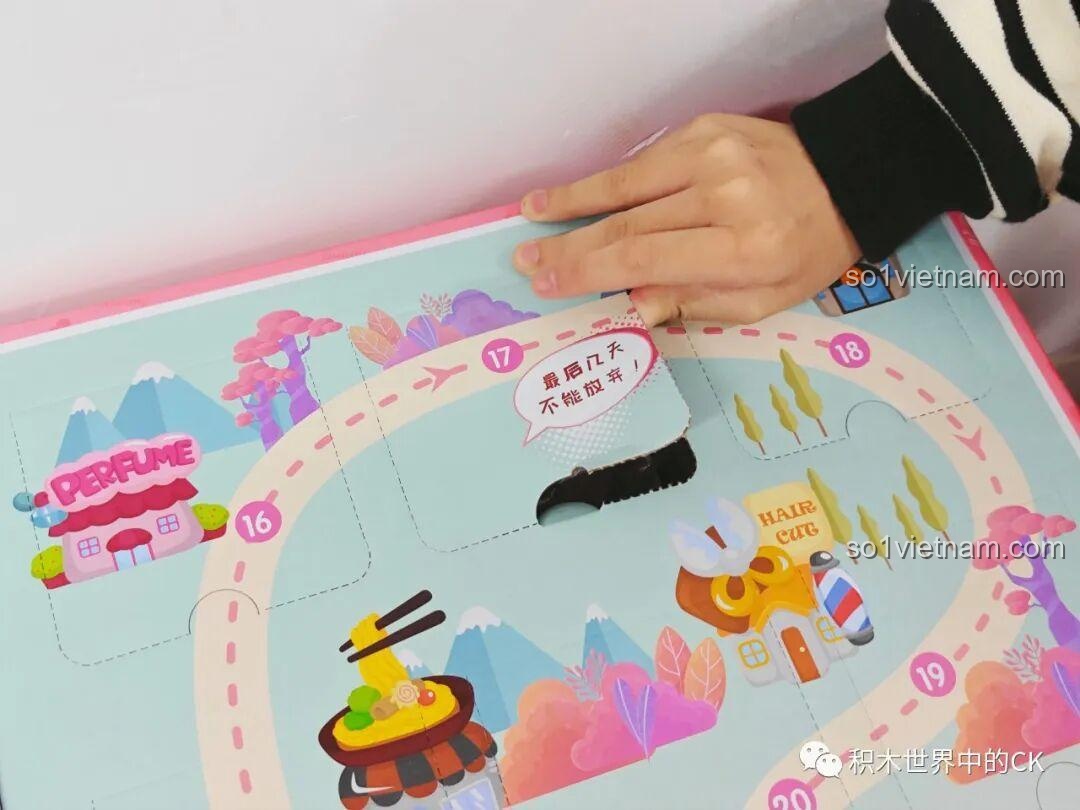 Một bé gái đang mở một ô cửa khác trên hộp QMAN 35018, thể hiện sự hấp dẫn của bộ lịch đếm ngược 21 ngày.