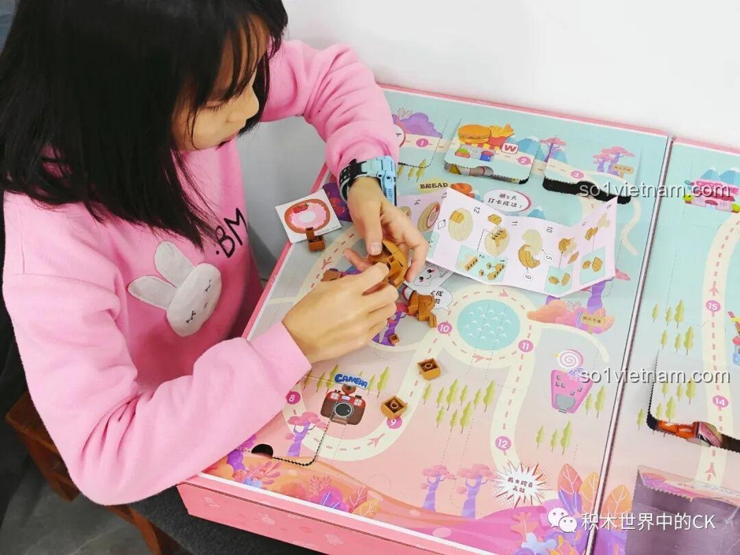 Bé gái đang lắp ráp mô hình sandwich từ các mảnh ghép màu nâu của bộ QMAN 35018, rèn luyện sự khéo léo.