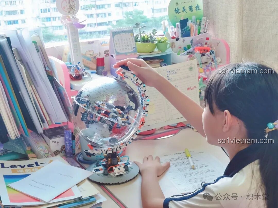 Một bé gái đang tương tác với mô hình Địa cầu Bình Minh JAKI CK003 trên bàn học, thể hiện tính giáo dục và giải trí của sản phẩm. Đồ chơi xây dựng Địa cầu Bình Minh JAKI CK 003 giá dân.