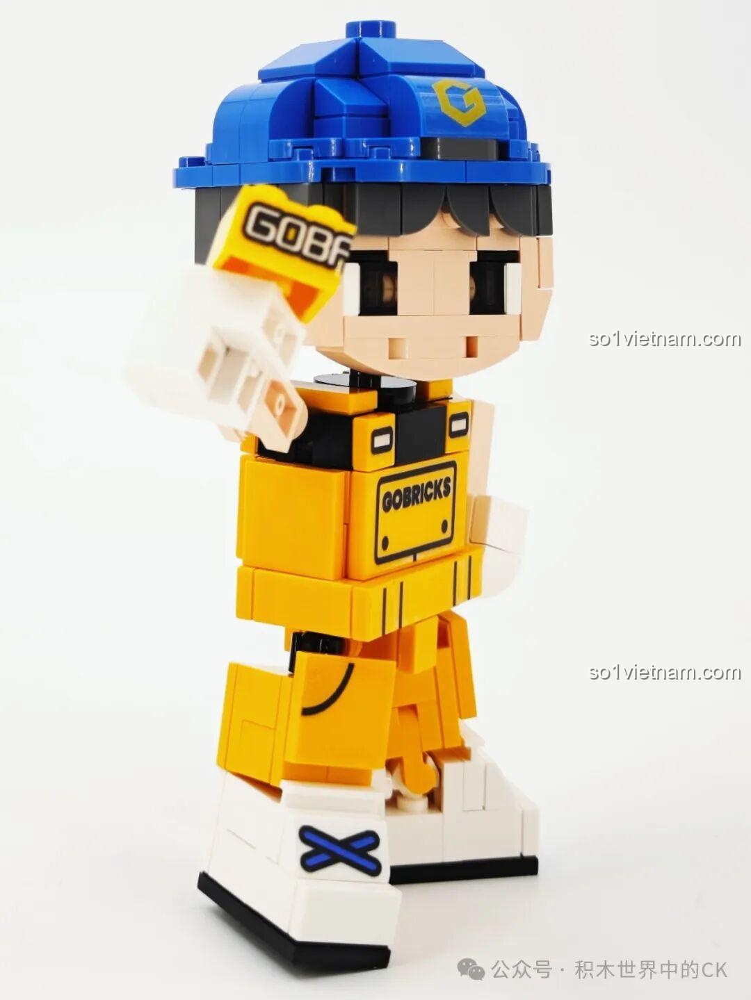 Gobricks G2411 Nhân vật lắp ghép màu vàng, đội mũ xanh, cầm viên gạch Gobricks, nhìn nghiêng