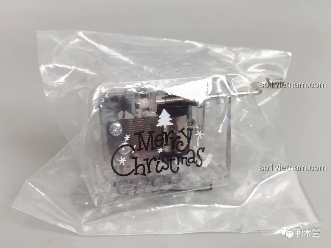 Cận cảnh hộp nhạc đi kèm trong bộ JAKI JK5128, có in chữ 'Merry Christmas' và hình cây thông.