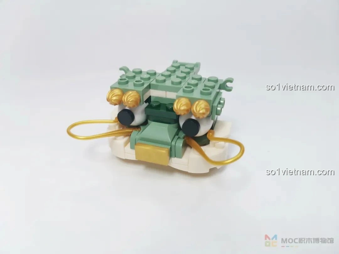 Phần đầu của mô hình JAKI JK20236 Kỳ Lân Chiêu Tài đang được lắp ráp, với đôi mắt lồi và các chi tiết in ấn.