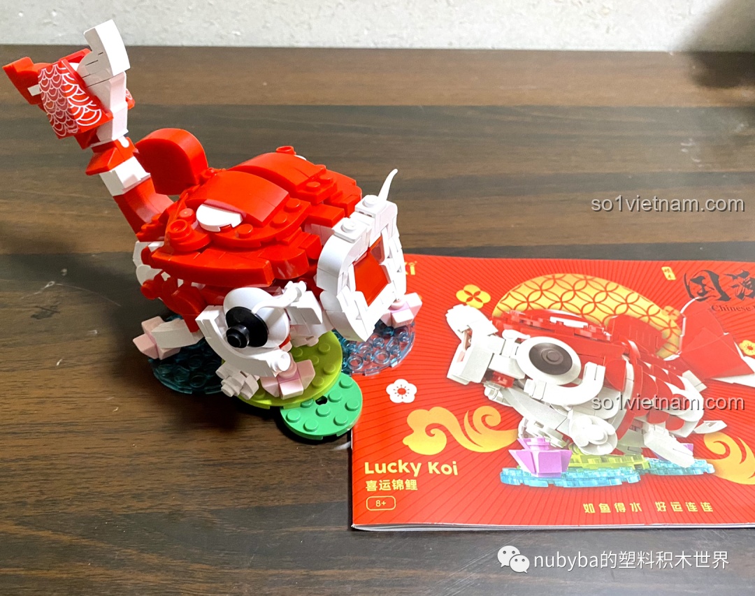 Mô hình JAKI Lucky Koi hoàn chỉnh được đặt cạnh hộp sản phẩm, cho thấy sự tương đồng và sống động của sản phẩm thực tế.