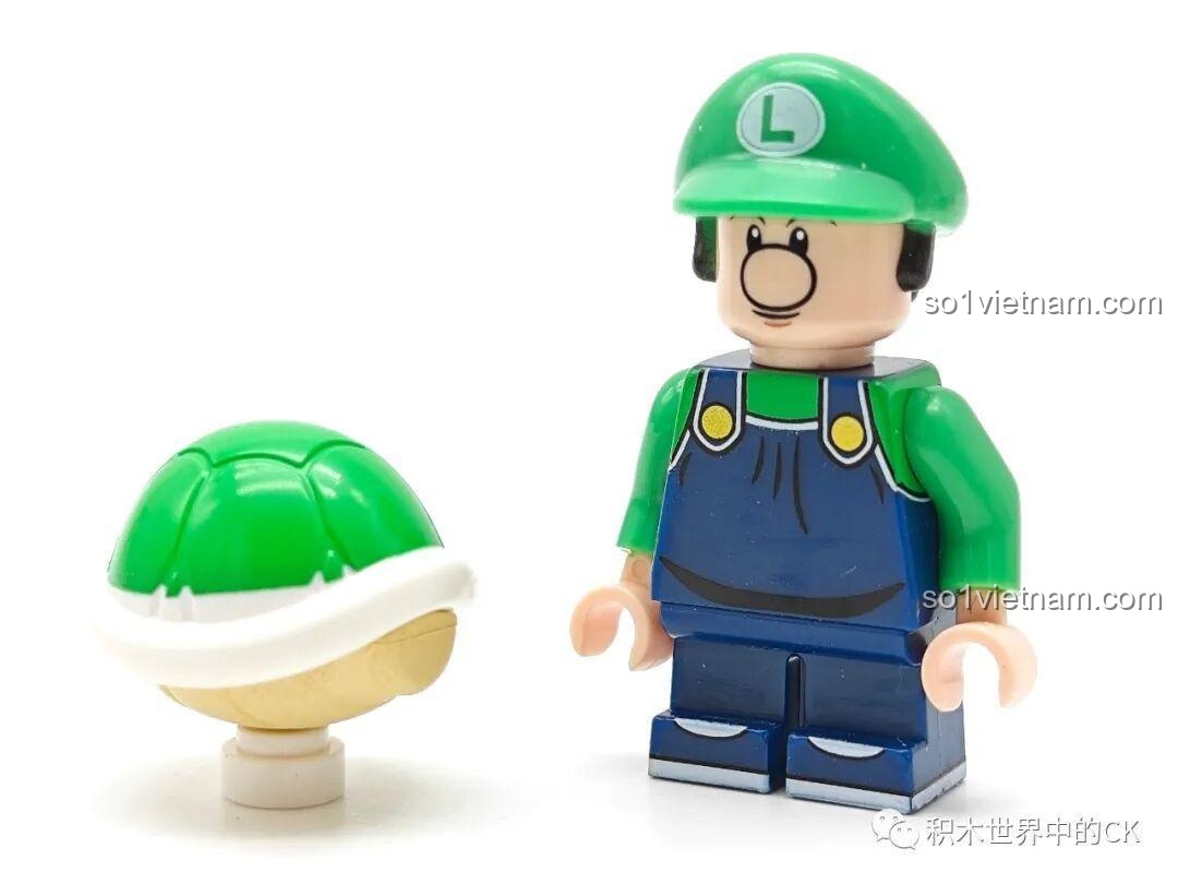 Minifigure Baby Luigi (K2115) từ set đồ chơi Baby Luigi KDL tiết kiệm, đứng cạnh Green Koopa Shell, nhìn từ phía trước.