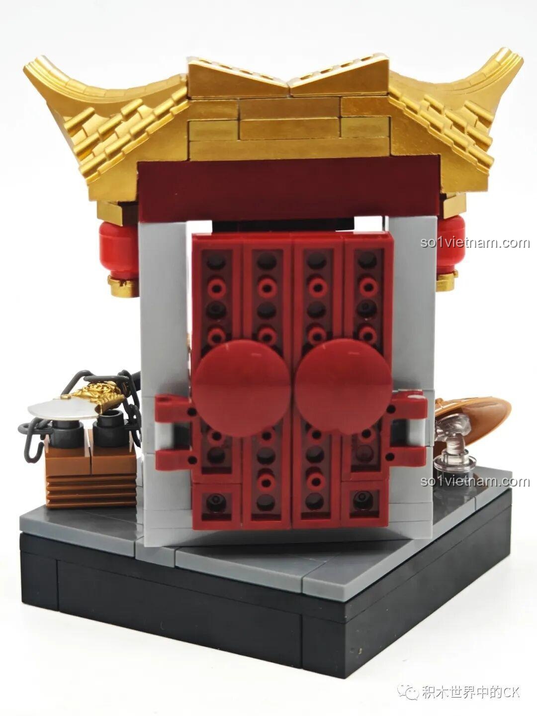 Mặt sau của mô hình cổng chùa, với thiết kế cửa đỏ và các chi tiết gạch xám.