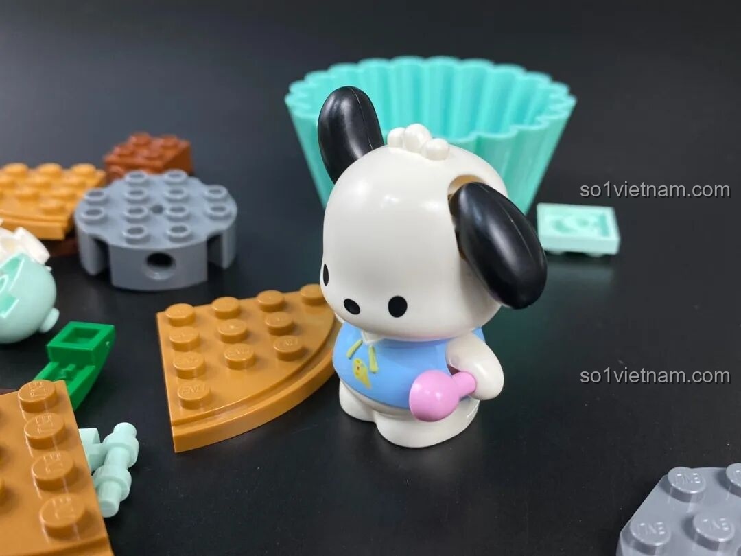 Minifigure Pochacco trong bộ cupcake, mặc áo xanh và cầm một viên kẹo hồng dễ thương.