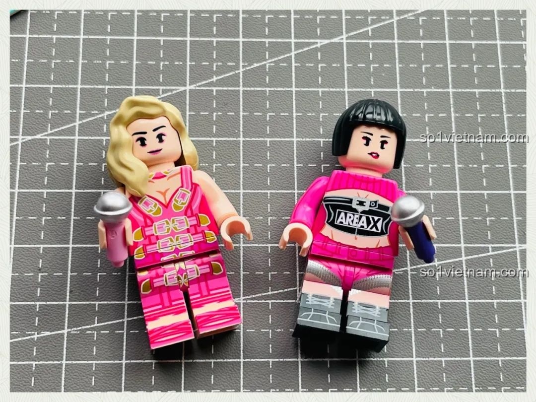 Hai minifigures ca sĩ tóc vàng và tóc đen của bộ lắp ráp Ái Vũ Đài AREA-X AB0006, cầm micro và mặc trang phục biểu diễn màu hồng.