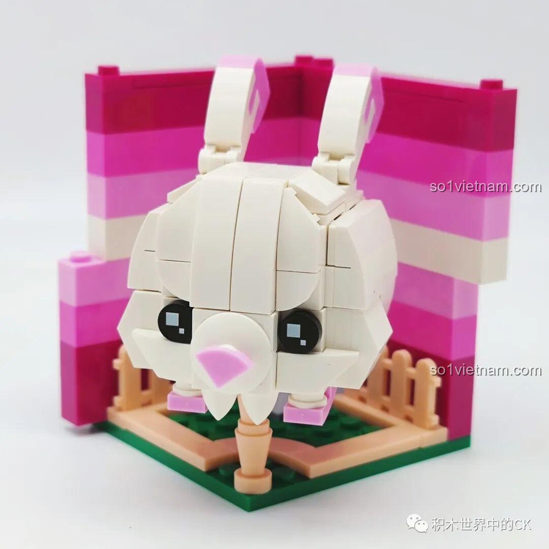 Mô hình lắp ráp Rubik hình thỏ trắng đã hoàn thiện, đặt trên một sa bàn nhỏ với hàng rào và nền màu hồng.