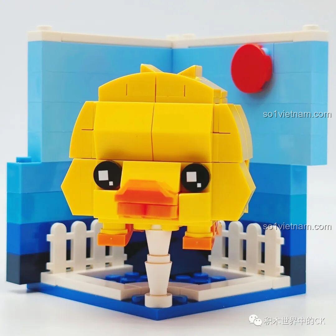 Mô hình lắp ráp Rubik Động Vật LQFUN hình vịt con màu vàng, có bối cảnh hàng rào trắng và nền trời xanh.