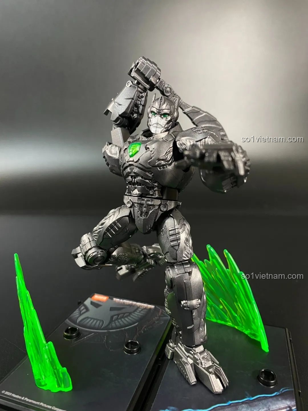 Mô hình Optimus Primal dạng robot tạo dáng chiến đấu với vũ khí trên đế trưng bày, đi kèm hiệu ứng năng lượng xanh.