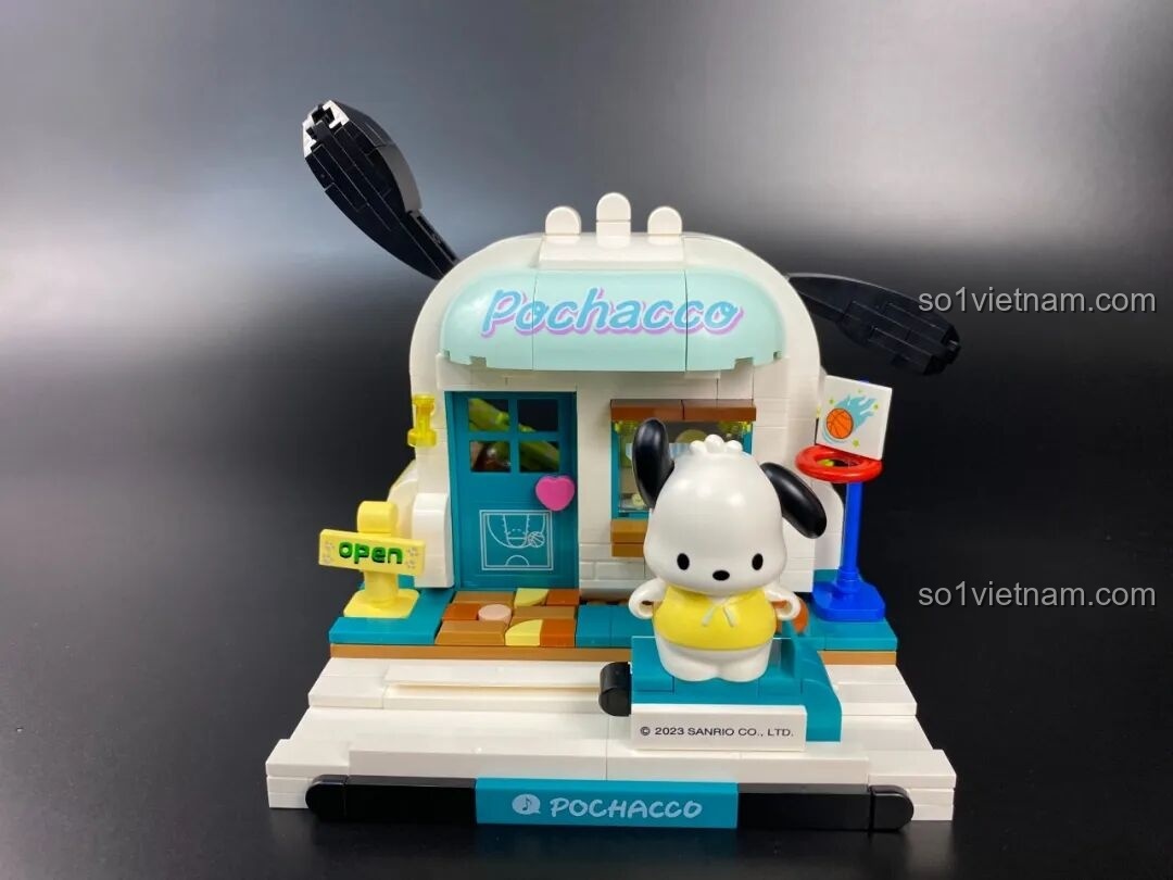 Minifigure Pochacco đứng tự hào trước cửa Nhà Thi Đấu Vui Vẻ do chính mình làm chủ, một hình ảnh hoàn thiện đẹp mắt.