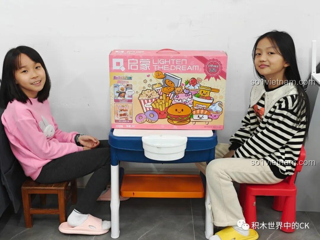 Hai bé gái hào hứng bên cạnh hộp quà bất ngờ QMAN 35018 chủ đề ẩm thực, một món quà tuyệt vời cho trẻ 6 tuổi.