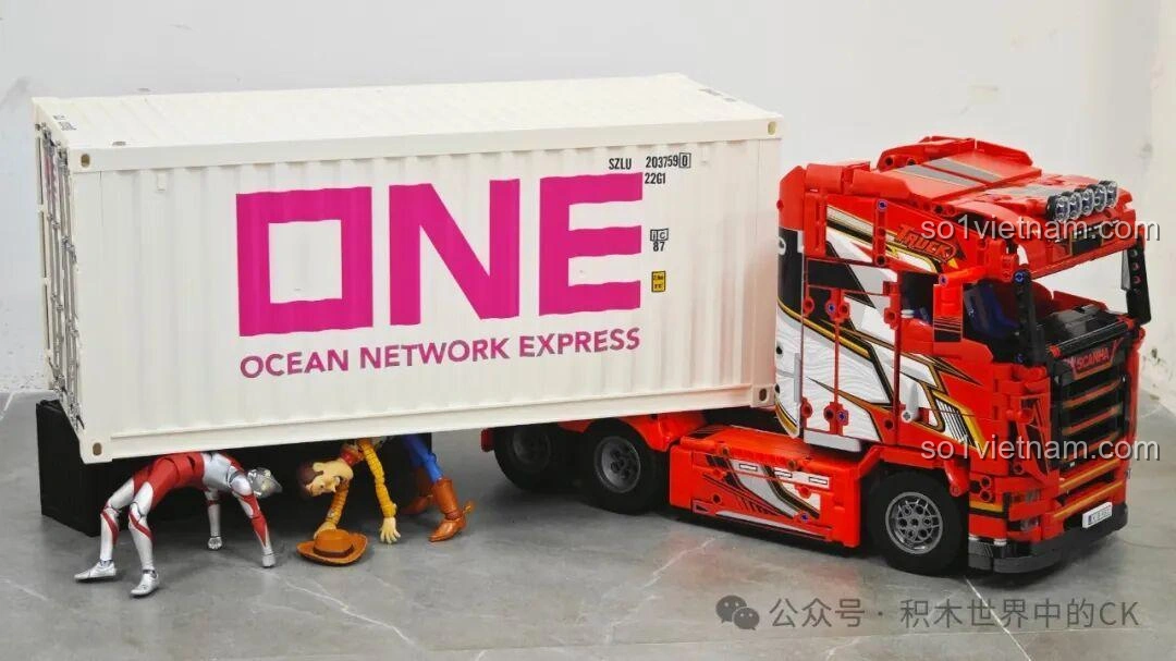 Mô hình Jie Star JJ9070 Xe Đầu Kéo Scania kéo container, nhìn từ góc khác, với các nhân vật đồ chơi.