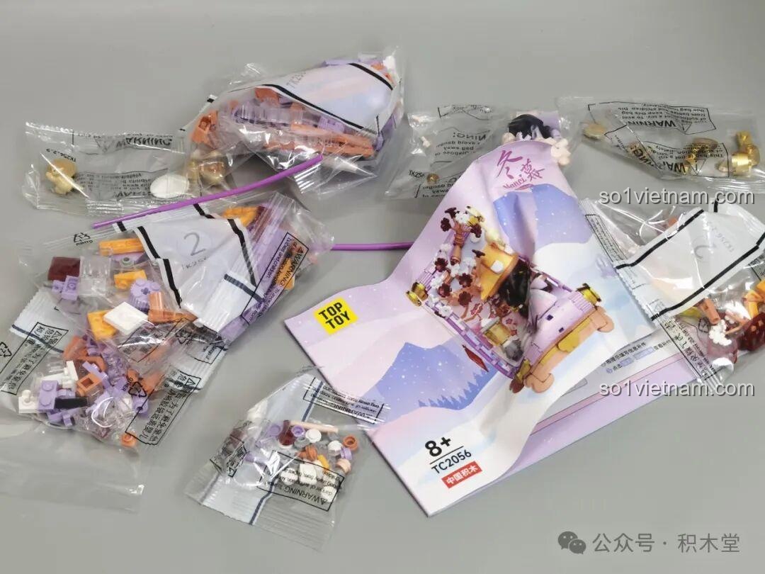 Bên trong hộp đồ chơi TOP TOY Nanci mùa Đông TC2056, với các túi mảnh ghép mang tông màu tím, trắng và cam.