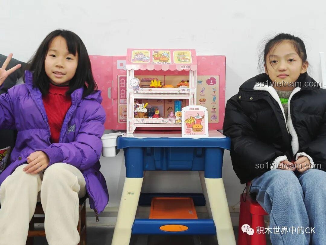 Hai bé gái tự hào khoe thành quả là bộ sưu tập 21 món ăn mini và kệ trưng bày QMAN 35018 đã hoàn thành.