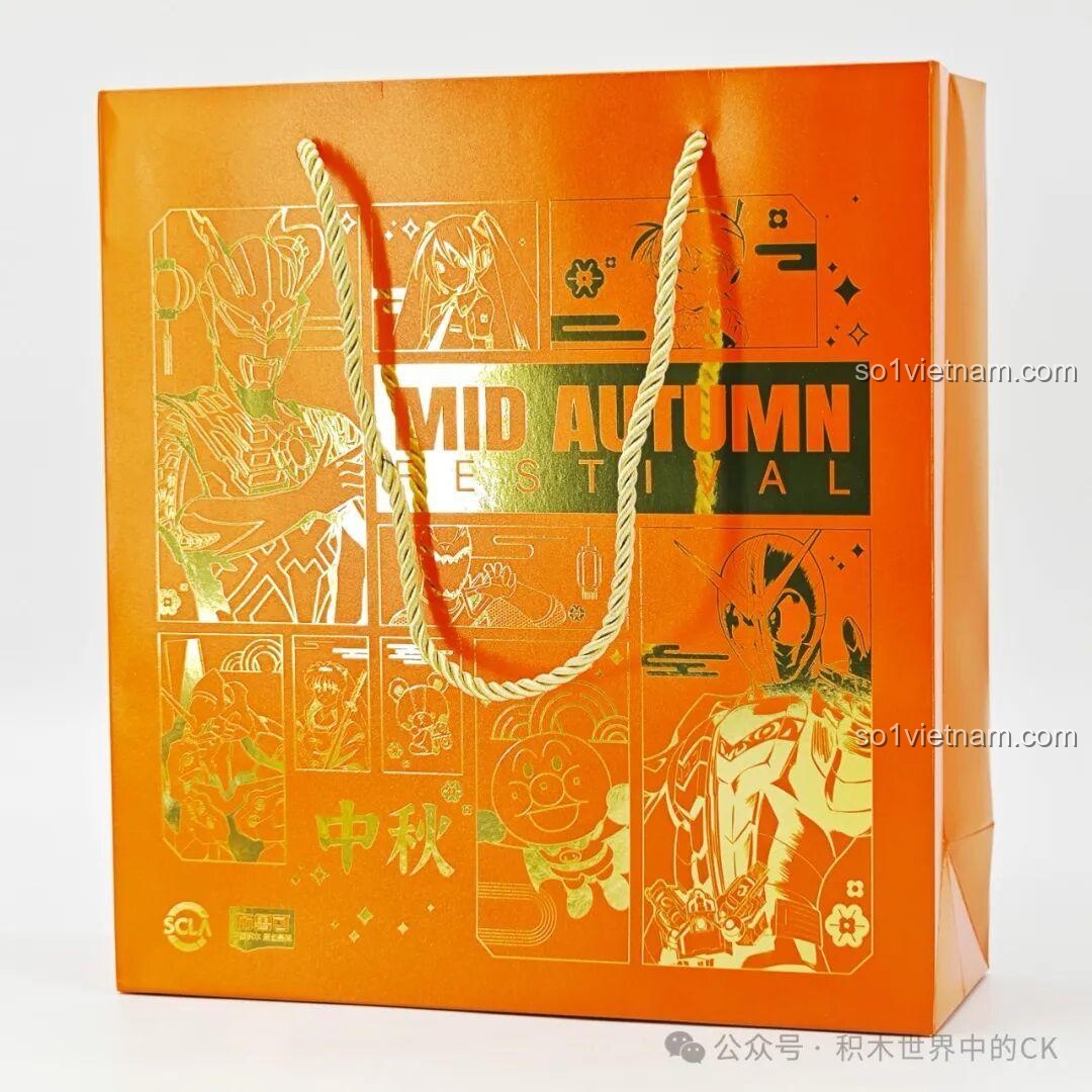 Túi giấy màu cam của hộp quà Trung Thu Ultraman và Kamen Rider với các hình in vàng lấp lánh, một món quà xịn cho bé trai 8 tuổi.